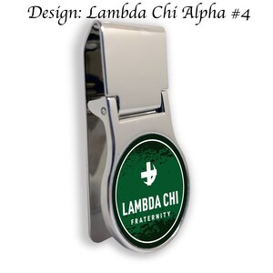 May include: A silver money clip with a round, green and white design. The design features a white cross and the text "Lambda Chi Fraternity".
