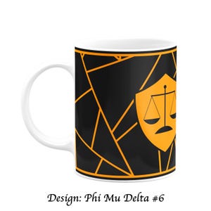 Puede incluir: Taza de cerámica blanca con un diseño geométrico negro y naranja. El diseño incluye un escudo con una balanza de la justicia y el texto "Design: Phi Mu Delta #6".