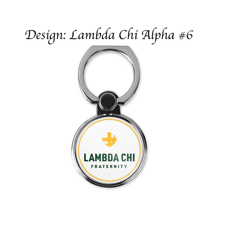May include: A silver phone ring holder with a white circle featuring a green and gold Lambda Chi Fraternity logo. The logo includes a cross and crescent moon.