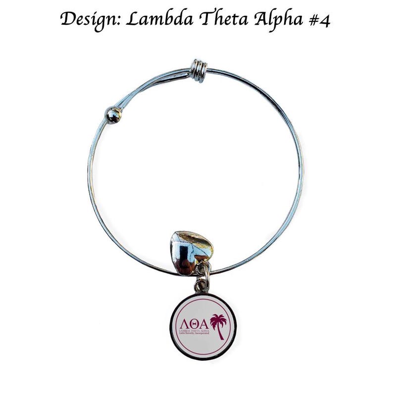 Puede incluir: Una pulsera de brazalete plateada con un dije en forma de coraz&oacute;n y un dije redondo con las letras "&Lambda;&Theta;A" y una palmera. El texto "Design: Lambda Theta Alpha #4" est&aacute; encima de la pulsera.