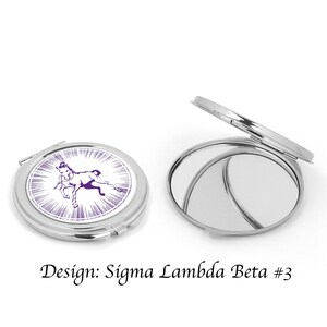 Pu&ograve; includere: Uno specchio compatto argentato con un design di cavallo viola e bianco. Il design include il testo "Sigma Lambda Beta #3".