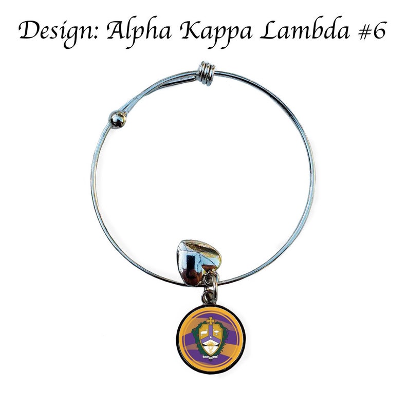 Puede incluir: Pulsera extensible de plata con un dije que presenta el escudo de la hermandad Alpha Kappa Lambda. El escudo es morado, dorado y blanco con una cruz y un escudo.
