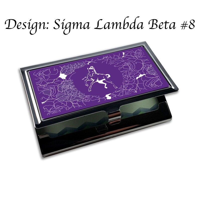Puede incluir: Un porta tarjetas de visita de metal morado con un dise&ntilde;o de caballo blanco y un patr&oacute;n blanco en espiral. El texto "Design: Sigma Lambda Beta #8" est&aacute; en la parte superior de la imagen.