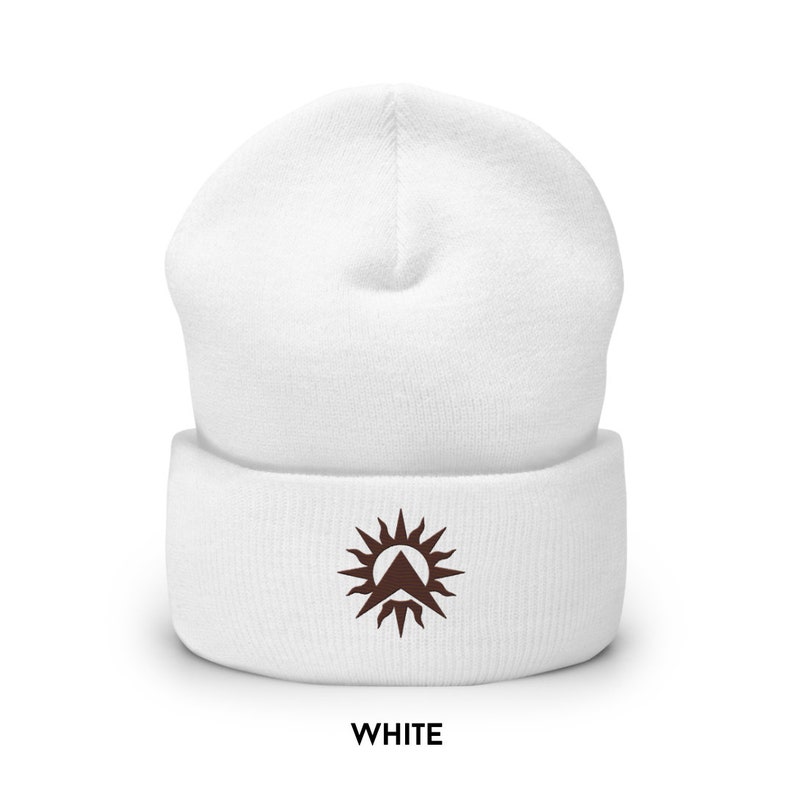 May include: White beanie hat with a brown embroidered sun and mountain design. The folded cuff displays the word "WHITE". A warm winter accessory for cold weather.