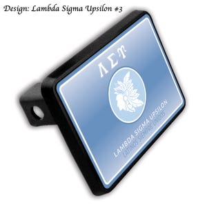 Op de afbeelding: Een zwarte trekhaakafdekking met een lichtblauwe achtergrond met de Griekse letters ΛΣΥ en een witte afbeelding van een persoon met een gevederde hoofdtooi. De tekst "LAMBDA SIGMA UPSILON LATINOS SIEMPRE UNIDOS" is ook afgebeeld.