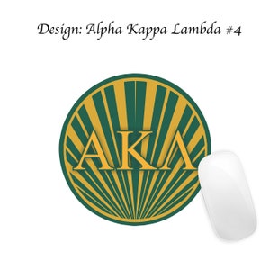 Pode incluir: Um tapete de rato redondo com um design de raios de sol verde e dourado. As letras "AKA" est&atilde;o em dourado no centro do design.