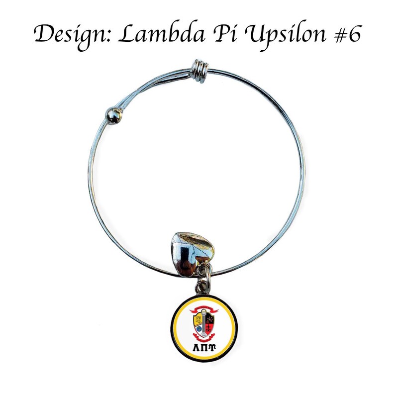 May include: A silver expandable bracelet with a charm featuring a yellow and black Lambda Pi Upsilon sorority crest. The charm has a black circle around the crest with the letters "&Lambda;&Pi;&Psi;" in white.