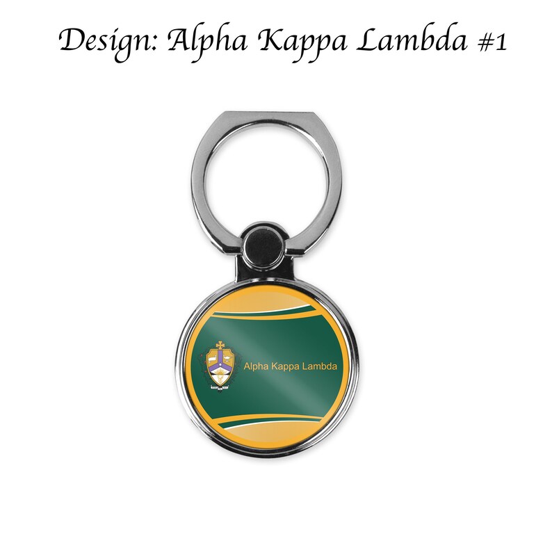 K&ouml;nnte beinhalten: Ein silberner Handy-Ringhalter mit einem runden, gr&uuml;n-goldenen Design. Das Design zeigt ein Wappen mit dem Text "Alpha Kappa Lambda".