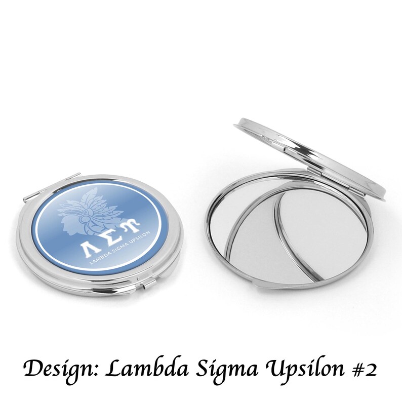 May include: A silver compact mirror with a blue and white design featuring the text "&Lambda;&Sigma;&Pi;" and a silhouette of a person wearing a headdress. The compact is open, revealing two mirrors. The text "Lambda Sigma Upsilon" is also visible.