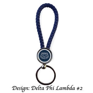 Könnte beinhalten: Ein marineblauer, geflochtener Leder-Schlüsselanhänger mit einem silberfarbenen Schlüsselring. Das kreisförmige Emblem zeigt ein weißes Design auf dunkelblauem Hintergrund. Der Text "Design: Delta Phi Lambda #2" befindet sich unten.