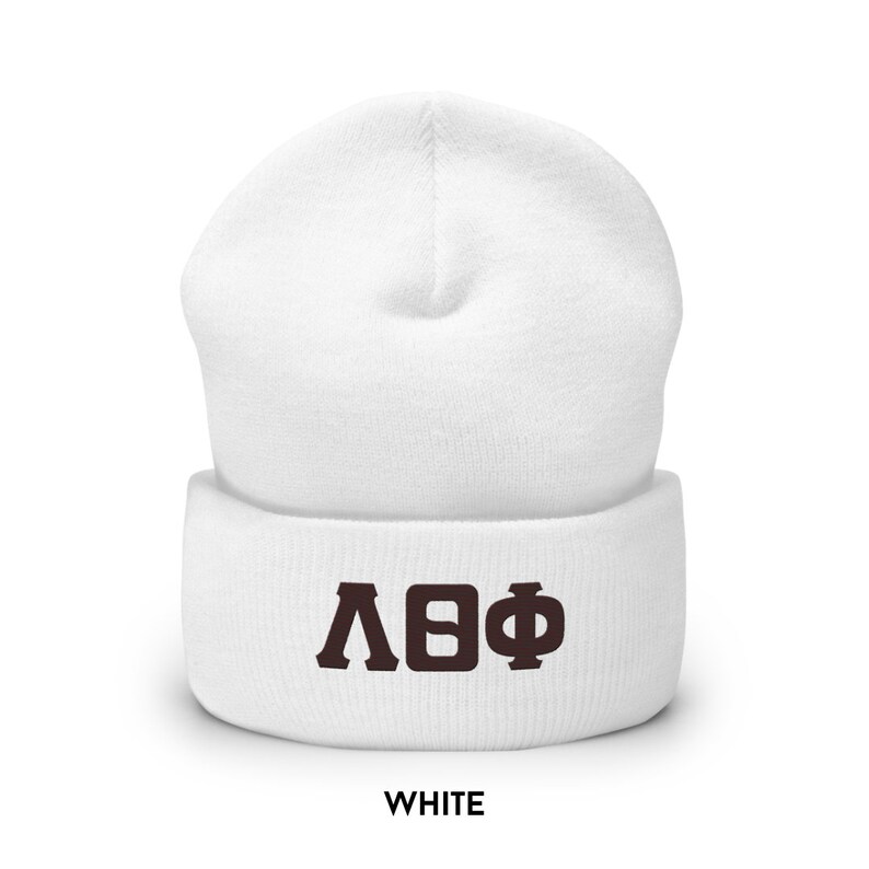 May include: A white beanie hat featuring the Greek letters &Lambda;&Theta;&Phi; in brown. The word "WHITE" is printed in white at the bottom of the image. The hat is made of a soft, knitted material.
