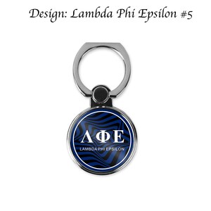 Może przedstawiać: Srebrny uchwyt do telefonu z okrągłym, niebiesko-czarnym wzorem. Wz&oacute;r zawiera białe litery, kt&oacute;re tworzą napis "&Lambda;&Phi;&Epsilon;" oraz słowa "Lambda Phi Epsilon".