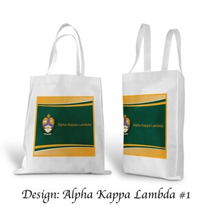 May include: Two white tote bags with green and gold designs. The design features a crest with the text "Alpha Kappa Lambda".