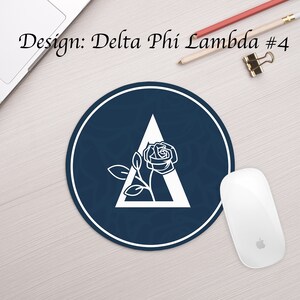 Może przedstawiać: Okrągła, ciemnoniebieska podkładka pod mysz z białym obramowaniem. W środku podkładki znajduje się biały tr&oacute;jkąt z białą r&oacute;żą w środku. Tekst "Design: Delta Phi' Lambda #4" znajduje się w g&oacute;rnej części obrazu.