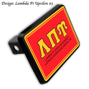 May include: Black trailer hitch cover featuring a red background with yellow Greek letters. The text "Lambda Pi Upsilon Sorority, Latinas Poderosas Unidas, Inc." is also visible. The design is labeled "Design: Lambda Pi Upsilon #3".