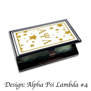 Peut inclure: Un porte-cartes de visite argent&eacute; avec un fond blanc et des &eacute;toiles dor&eacute;es ainsi que les lettres "AYA" en or.