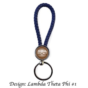 Op de afbeelding: Een marineblauwe gevlochten leren sleutelhanger met een zilveren sleutelring. De sleutelhanger heeft een rond embleem met de Griekse letters ΛΘΦ in wit. De tekst "Lambda Theta Phi" is ook zichtbaar.