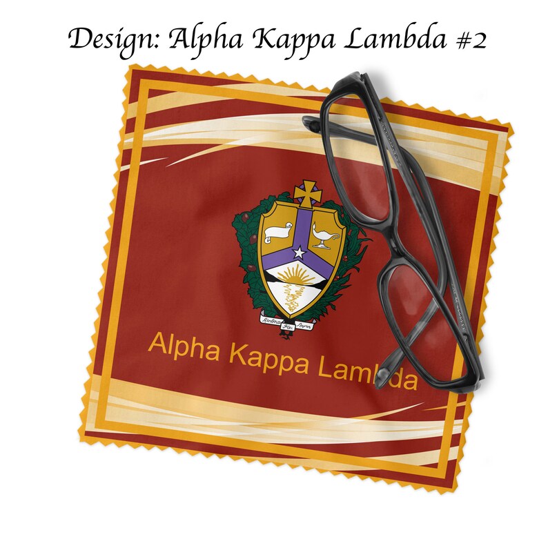 K&ouml;nnte beinhalten: Ein rotes, goldenes und violettes Mikrofaser-Reinigungstuch mit dem Wappen von Alpha Kappa Lambda und dem aufgedruckten Schriftzug "Alpha Kappa Lambda". Eine schwarze Brille liegt auf dem Tuch.