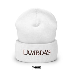 May include: A white beanie hat with the word "LAMBDAS" embroidered in brown. The word "WHITE" is printed below the hat in a bold font. The hat is made of a soft, knitted material.