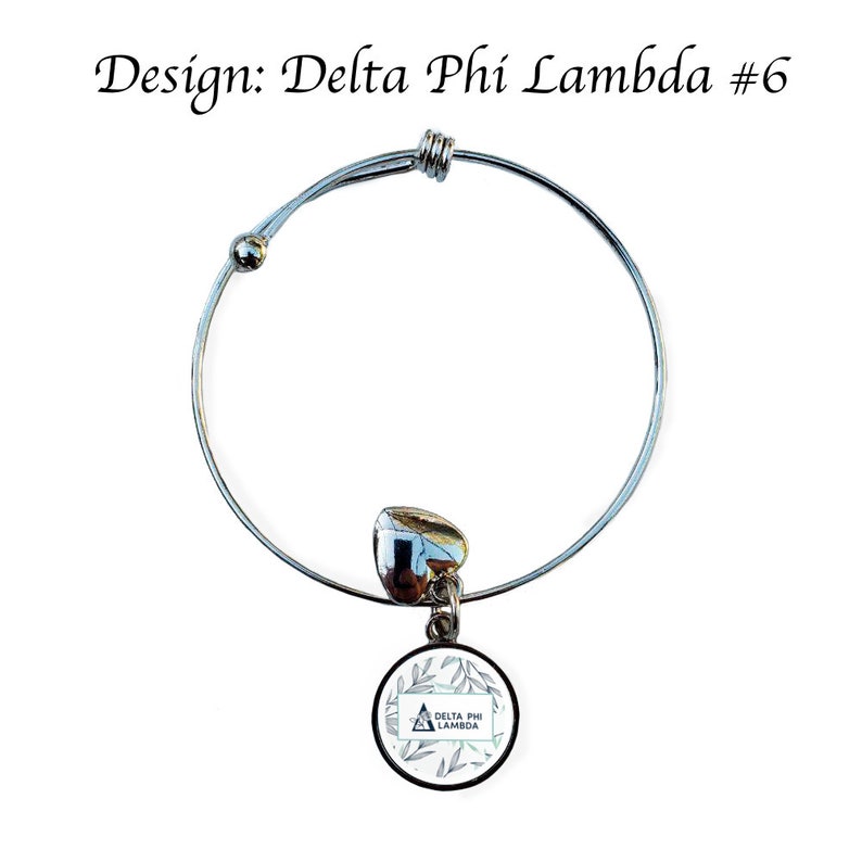 K&ouml;nnte beinhalten: Silbernes, ausziehbares Armband mit einem Anh&auml;nger in Form eines wei&szlig;en Kreises mit gr&uuml;nem Blattdesign und dem Text "Delta Phi Lambda".
