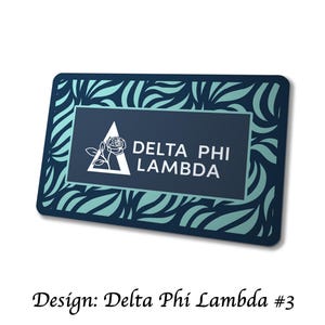 May include: Rectangular navy blue and teal design with the text "DELTA PHI LAMBDA". The design features a white triangle with a rose and the text is in white. The border has a teal and navy blue pattern.