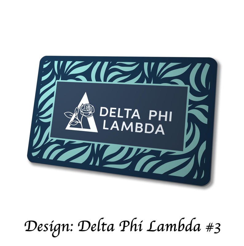 May include: Rectangular navy blue and teal design with the text "DELTA PHI LAMBDA". The design features a white triangle with a rose and the text is in white. The border has a teal and navy blue pattern.