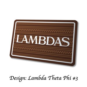 Puede incluir: Una pegatina rectangular marr&oacute;n con la palabra "LAMBDAS" en letras blancas. La pegatina tiene un borde blanco y un dise&ntilde;o de l&iacute;neas horizontales y zigzags. El texto "Design: Lambda Theta Phi #3" est&aacute; debajo.
