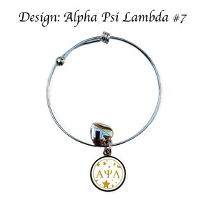 May include: A silver expandable bracelet with a charm featuring a white circle with gold stars and the letters "&Alpha;&Psi;&Lambda;" in gold.