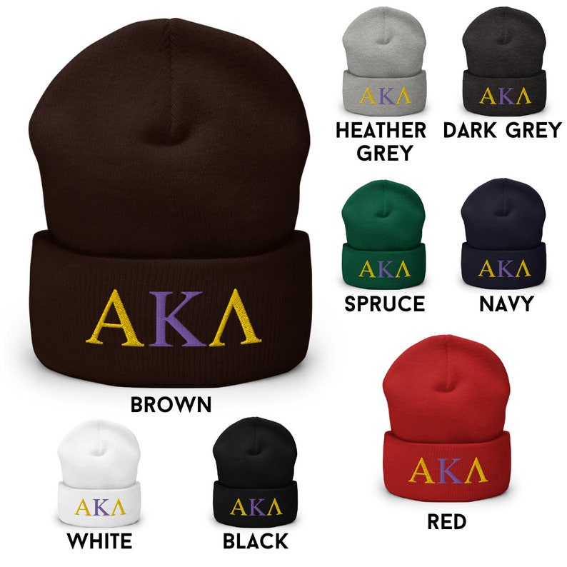 Op de afbeelding: Een verzameling van tien beanies in verschillende kleuren, waaronder bruin, wit, zwart, rood, donkergrijs, grijs met een vleugje kleur, marineblauw en spar. Elke beanie heeft de letters "AKA" geborduurd in goud en paars.