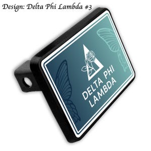 May include: Black trailer hitch cover with a teal and white design. The design features a white triangle with a rose and the text "DELTA PHI LAMBDA". Butterfly wing outlines are visible in the background. The text "Design: Delta Phi Lambda #3" is at the top.