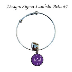 K&ouml;nnte beinhalten: Ein silbernes, ausziehbares Armband mit einem lilafarbenen Anh&auml;nger mit den Buchstaben "&Sigma;&Lambda;&Beta;" und dem Text "Sigma Lambda Beta International Fraternity".