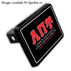 May include: A black trailer hitch cover with a rectangular design. The design features the Greek letters &Alpha;&Pi;&Upsilon; in red, with the text "LAMBDA PI UPSILON SORORITY, LATINAS PODEROSAS UNIDAS, INC. Empowered Women, Empowering Women." in white.