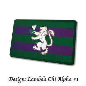 May include: Rectangular green and purple design with a white lion holding a white flower. The text "Design: Lambda Chi Alpha #1" is at the bottom. The design has a green background with two purple stripes.