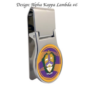 Peut inclure: Un porte-monnaie en argent avec un design rond et coloré représentant un bouclier violet avec une colombe blanche, une étoile et un phénix. Le bouclier est entouré d'une couronne de laurier verte et d'un fond jaune et orange.