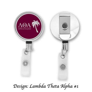 May include: Two badge reels featuring a Lambda Theta Alpha design. The front reel has a maroon background with white text and a palm tree graphic. The back reel is silver with a clip. The text "Design: Lambda Theta Alpha #1" is at the bottom.