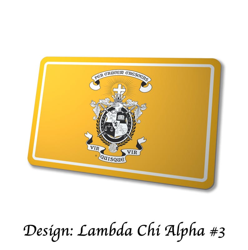 May include: A rectangular yellow item with a white border, featuring a crest with a cross, scales, and a book. The text "PER CRUCEM CRESCENS" is above the crest, and "VIR QUISQUE VIR" is below. The text "Design: Lambda Chi Alpha #3" is at the bottom.