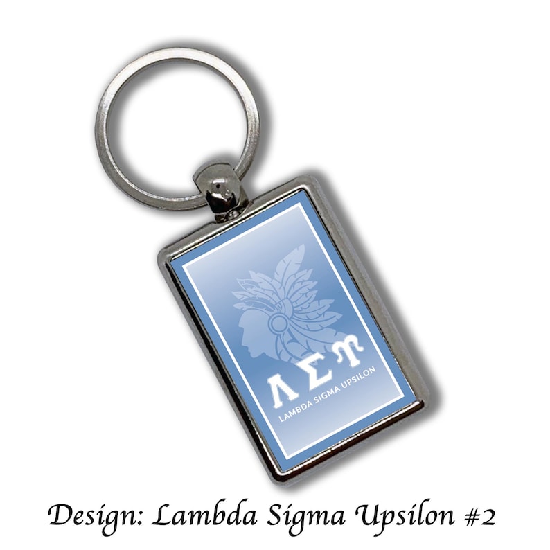 May include: Silver rectangular keychain with a light blue background. The keychain features a white graphic of a profile with a feathered headdress and the Greek letters &Lambda;&Sigma;&Pi;. The text "LAMBDA SIGMA UPSILON" is also present.
