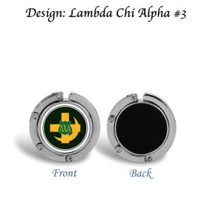 Può includere: Due appendini per borse color argento. Il lato anteriore presenta un emblema verde e oro con la scritta "ΛXA" e un disegno a croce. Il lato posteriore è nero. Il testo "Design: Lambda Chi Alpha #3" è in alto.