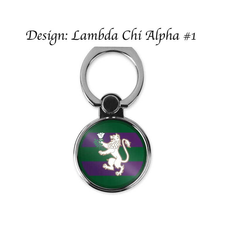 May include: A silver phone ring holder with a round, green and purple design featuring a white lion holding a white flower. The design says "Lambda Chi Alpha #1".