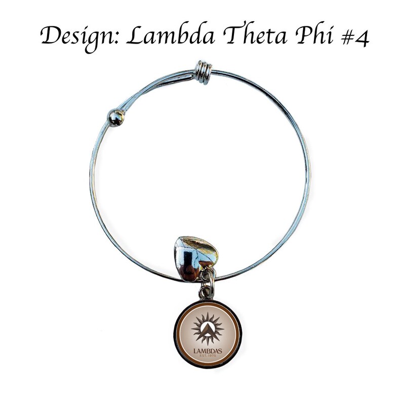 Op de afbeelding: Een zilveren uittrekbaar armband met een bedel met een bruin en wit logo met de tekst "Lambdas Est. 1913".