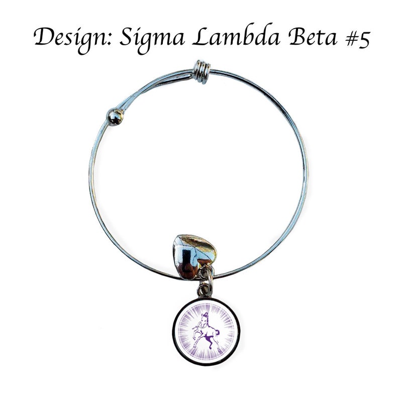 K&ouml;nnte beinhalten: Ein silbernes, ausziehbares Armband mit einem Anh&auml;nger, der ein Pferd in Lila und Wei&szlig; zeigt. Der Anh&auml;nger ist mit einem silbernen herzf&ouml;rmigen Verbinder am Armband befestigt. Das Armband tr&auml;gt den Text "Design: Sigma Lambda Beta #5" auf wei&szlig;em Hintergrund.