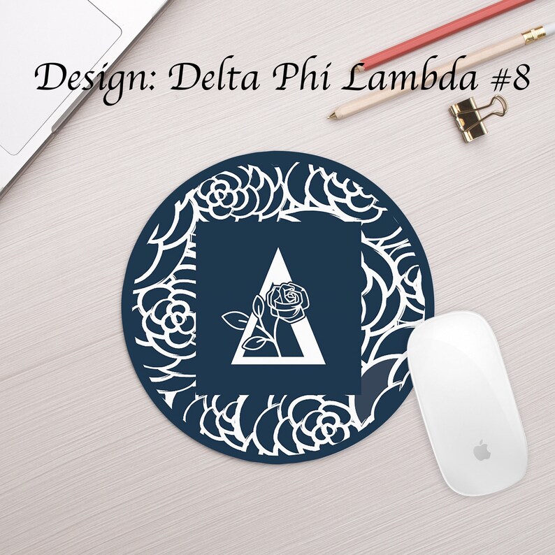 Może przedstawiać: Okrągła podkładka pod mysz w kolorze granatowym z białym wzorem kwiatowym i białym tr&oacute;jkątem z r&oacute;żą w środku. Tr&oacute;jkąt zawiera literę "A". Tekst "Design: Delta Phi Lambda #8" znajduje się w g&oacute;rnej części obrazu.