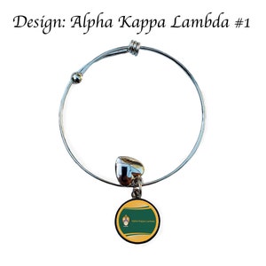 Puede incluir: Un brazalete extensible de plata con un dije circular verde y dorado con el texto "Alpha Kappa Lambda" en &eacute;l.