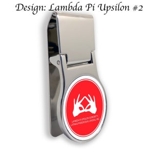 Op de afbeelding: Een zilveren geldclip met een rode cirkel met een wit handsymbool en de tekst "LAMBDA PI UPSILON SORORITY, LATINAS PODEROSAS UNIDAS, INC."