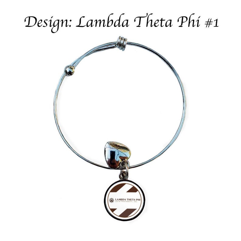 Op de afbeelding: Een zilveren uittrekbare armband met een bedel met een witte en bruine cirkel met de tekst "Lambda Theta Phi Latin Fraternity, Inc." De bedel is bevestigd aan een zilveren hart.