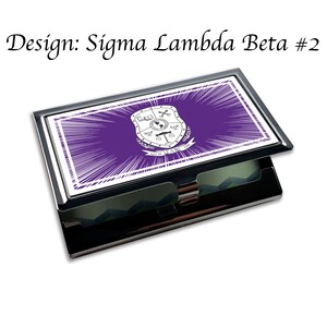 Puede incluir: Un porta tarjetas de plata con un dise&ntilde;o morado y blanco. El dise&ntilde;o presenta un escudo con las letras "&Sigma;&Lambda;&Beta;" y el texto "April 26, 1900".