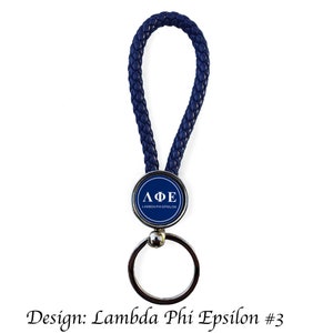 May include: A navy blue braided leather keychain with a silver key ring. The round emblem features the Greek letters ΛΦΕ in white on a navy blue background. The text "Lambda Phi Epsilon" is below the letters.