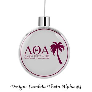 May include: A white Christmas ornament with a silver top and a clear, round, glass front. The ornament features a burgundy palm tree and the letters "ΛΘΑ" with the text "Lambda Theta Alpha Latin Sorority, Incorporated" below.