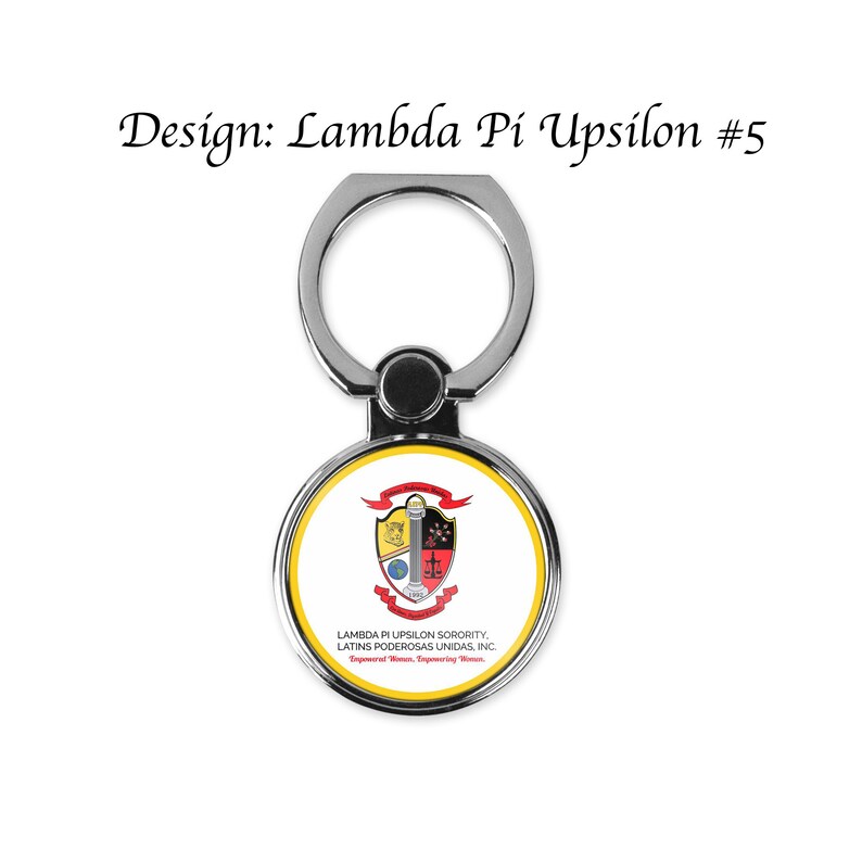 Op de afbeelding: Een zilveren telefoonringhouder met een ronde, witte en gele sticker met een wapenschild met een pilaar, een wereldbol, een weegschaal en een zwaard. De tekst op de sticker luidt "Lambda Pi Upsilon Sorority, Latins Poderosas Unidas, Inc. Empowering Women, Inspiring Women."