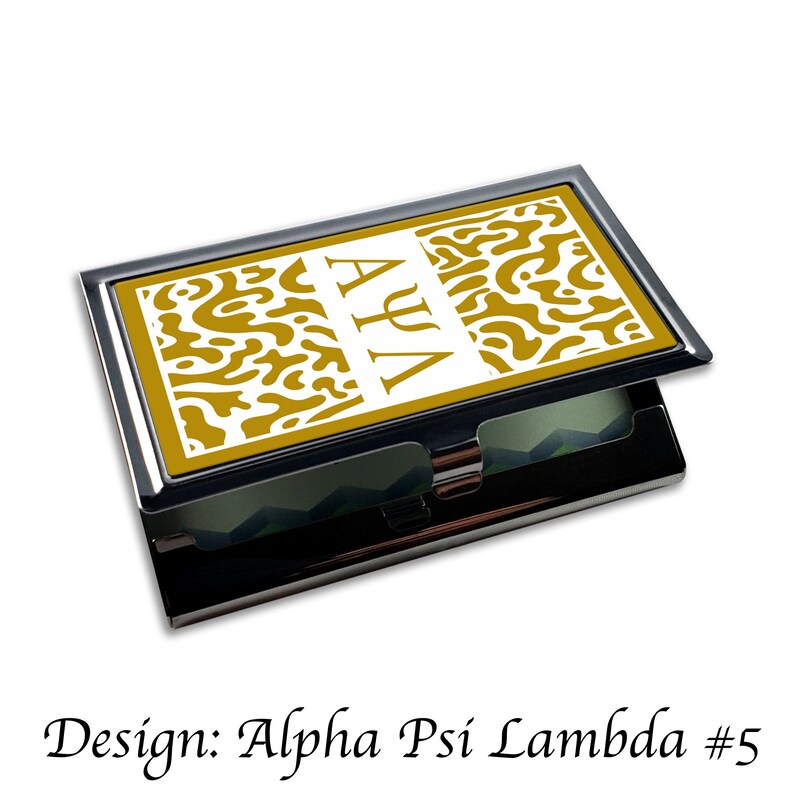 Peut inclure: Un porte-cartes de visite or et blanc avec une bordure argent&eacute;e. Le devant du porte-cartes pr&eacute;sente un fond blanc avec un motif abstrait dor&eacute; et les lettres "&Alpha;&Psi;&Lambda;" en blanc.